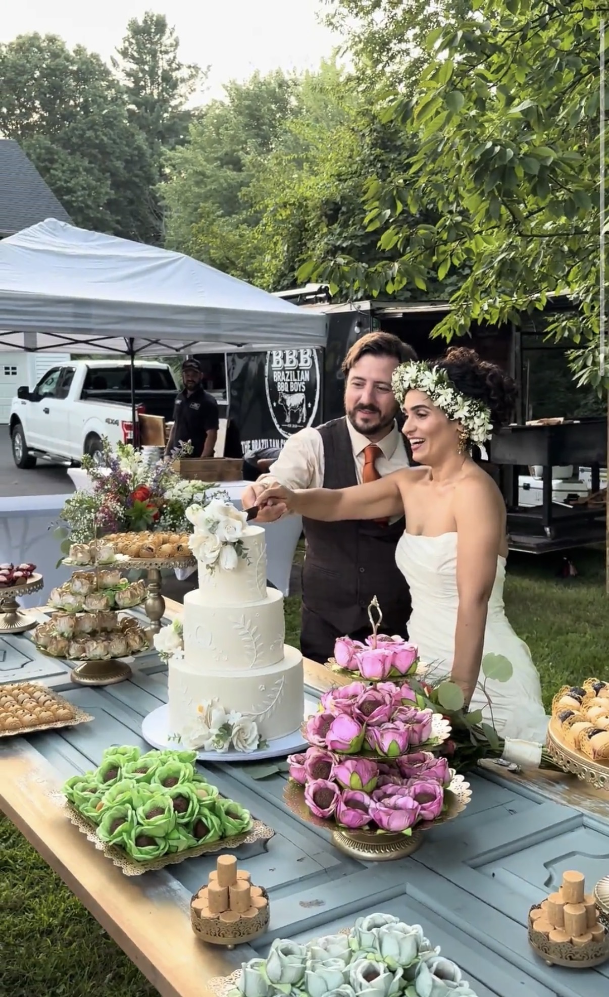 Couple cutting their wedding cake with Brazilian BBQ Boys catering setup in the background